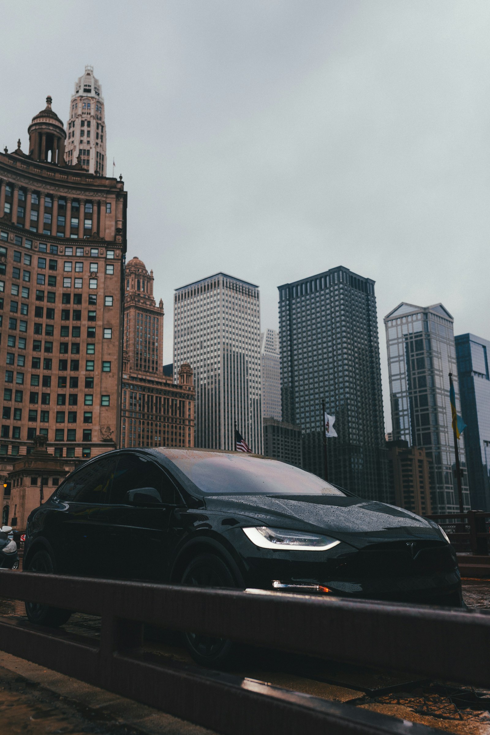 Black car parked along the Chicago River with downtown towers behind it